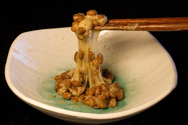 Natto in a bowl being held up by chopsticks.